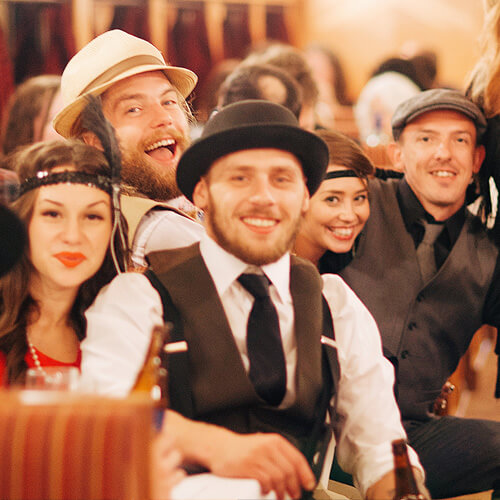 A group of smiling people dressed in roaring 20s outfits pause