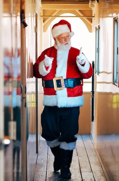 A man dressed as Santa walks down a train corridor