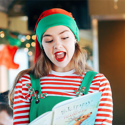 A young woman dressed as an elf reads from a Christmas book