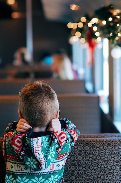 A young boy in a Christmas sweater looks away from the camera in a train car decorated for the holiday