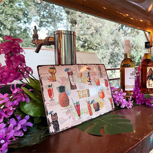 A tiki menu leans against a bar decorated with tropical flowers