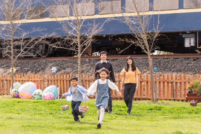 Family with two kids running on grass near painted eggs and train.