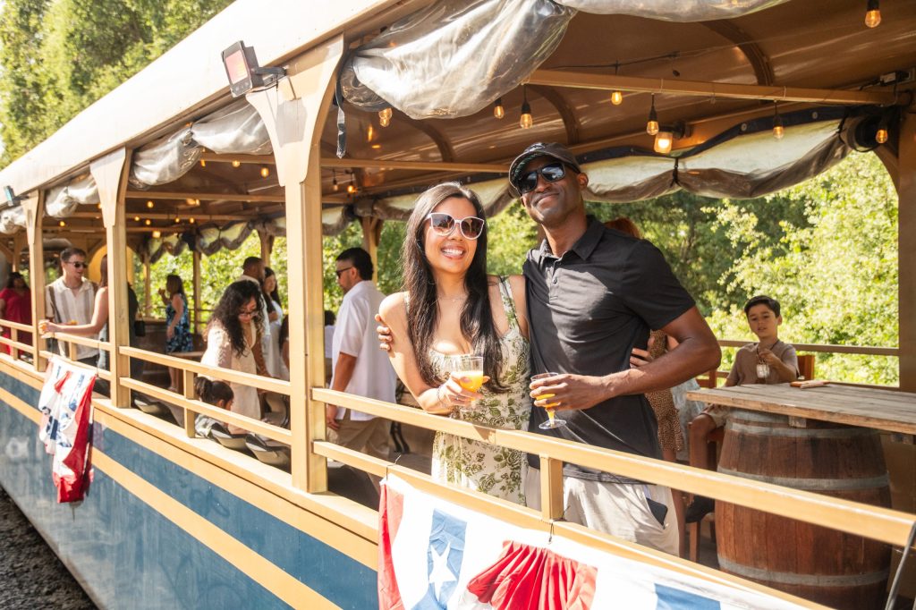 Couple posing on a decorated train with other passengers in the background.