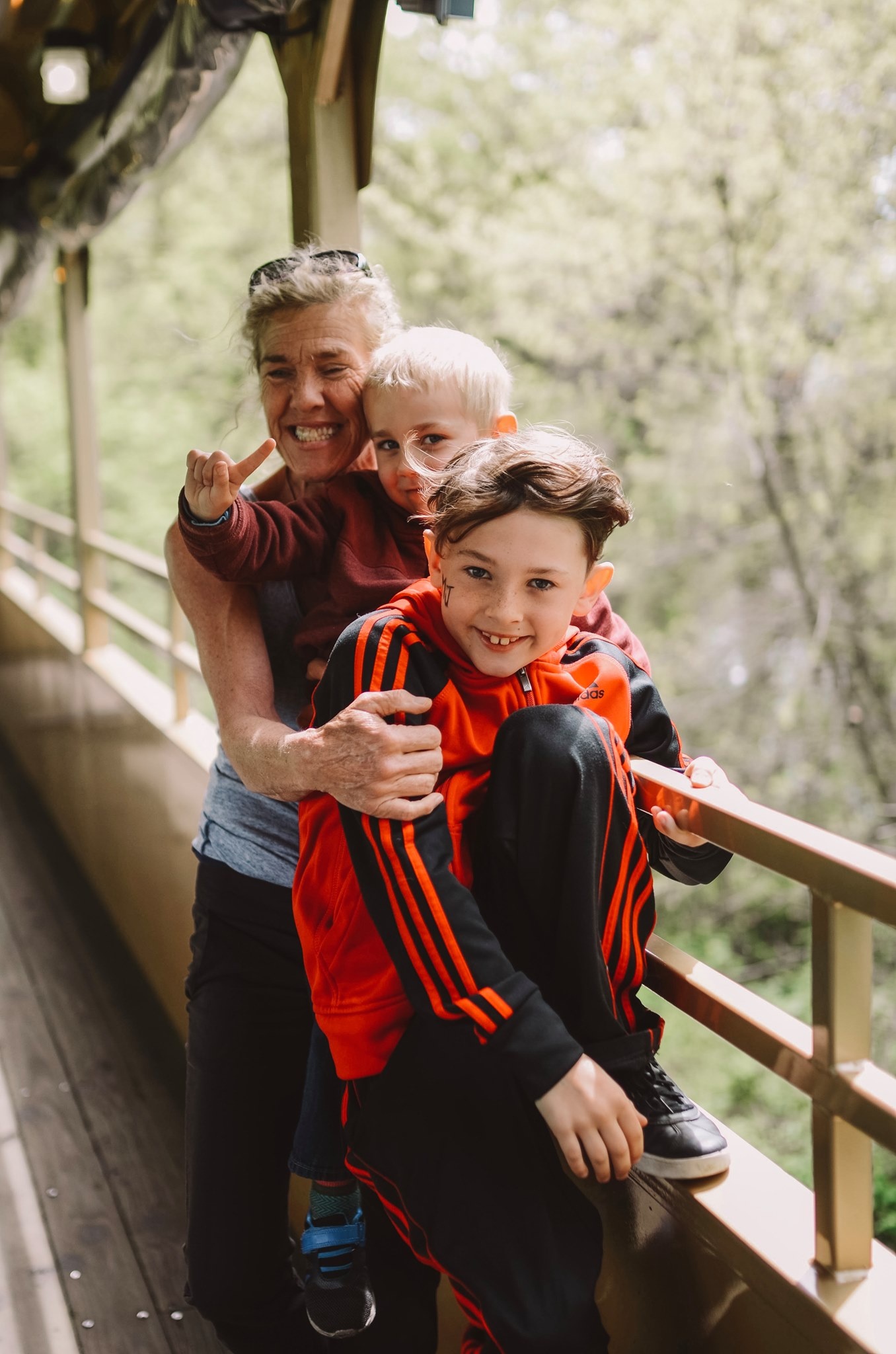 Smiling woman hugs two children on a wooden bridge.