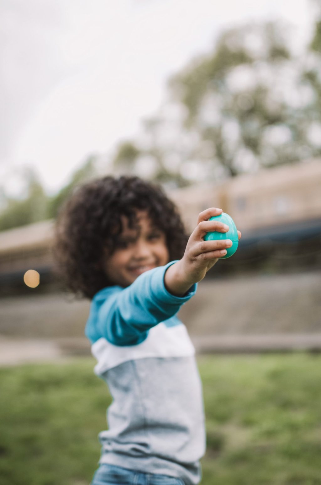 Child holding a blue ball in a park with a blurred background.