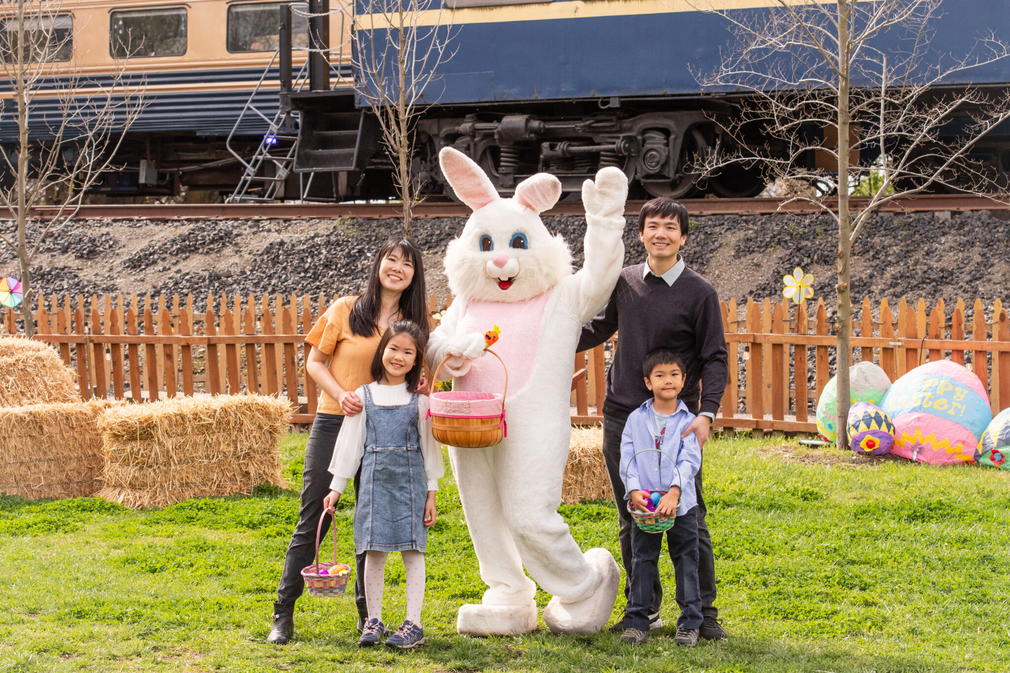 Family posing with Easter Bunny near train, holding baskets.