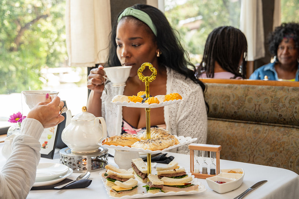 Woman sipping tea at a table with sandwiches and pastries