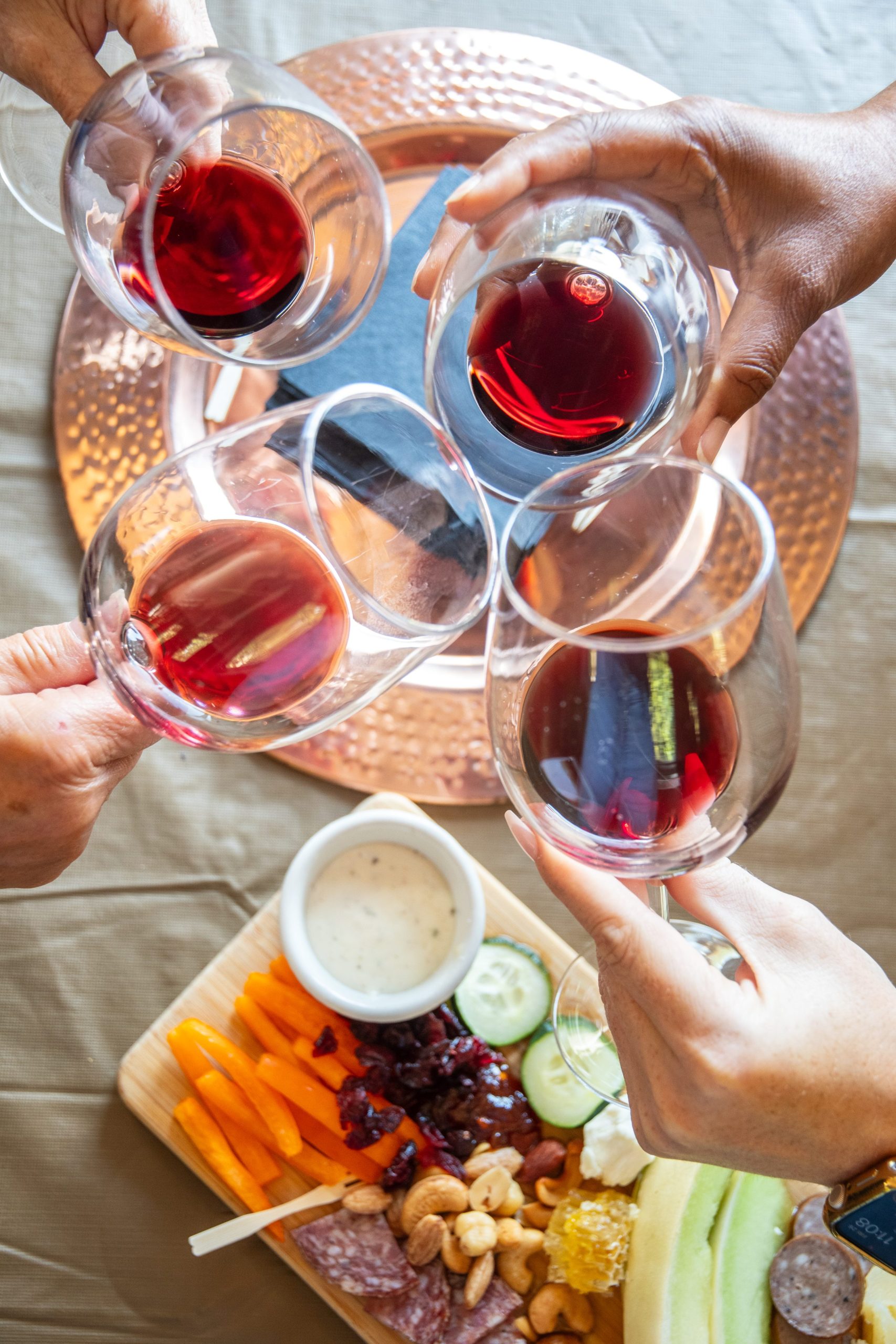 Four glasses of red wine toasting above a platter with snacks.