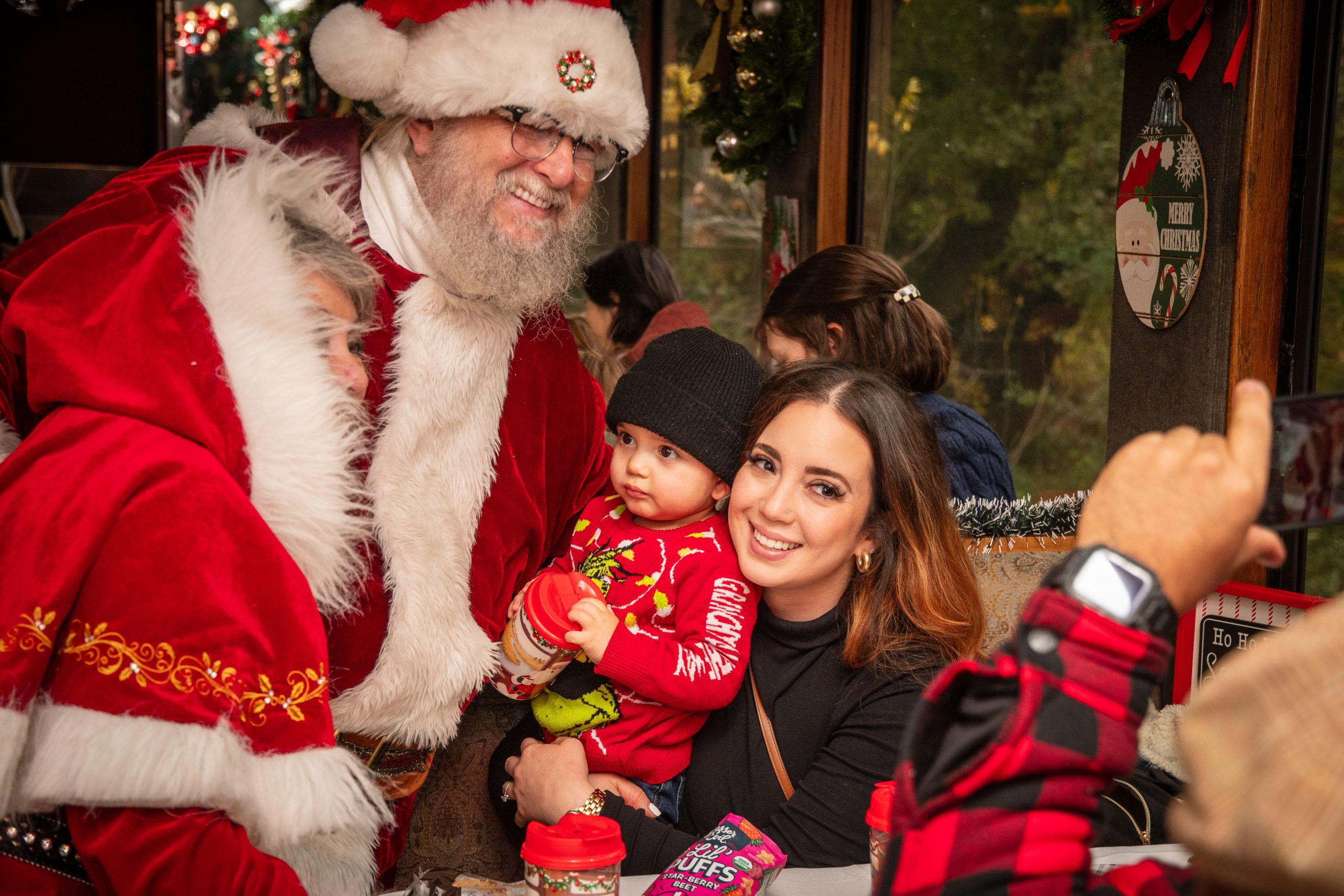 Santa with family posing for a festive photo, with a baby in red and a smiling woman.