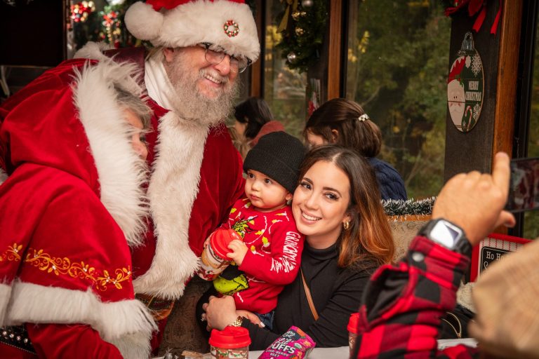 Santa with family posing for a festive photo, with a baby in red and a smiling woman.