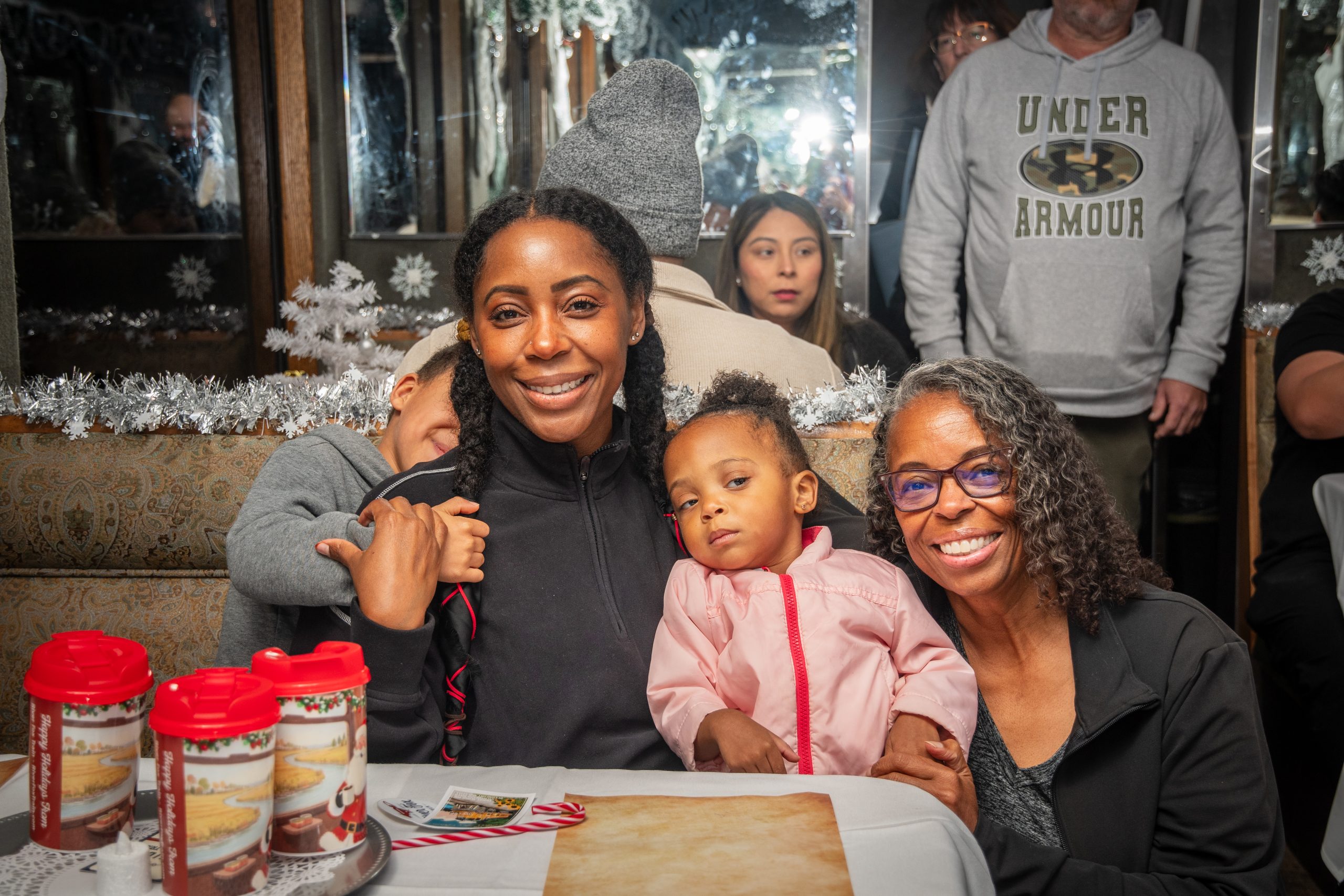Group of people smiling at a decorated holiday table with hot drink cups.