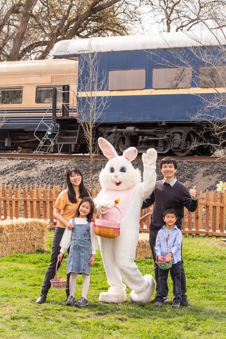 Family with Easter Bunny near train and hay bales.