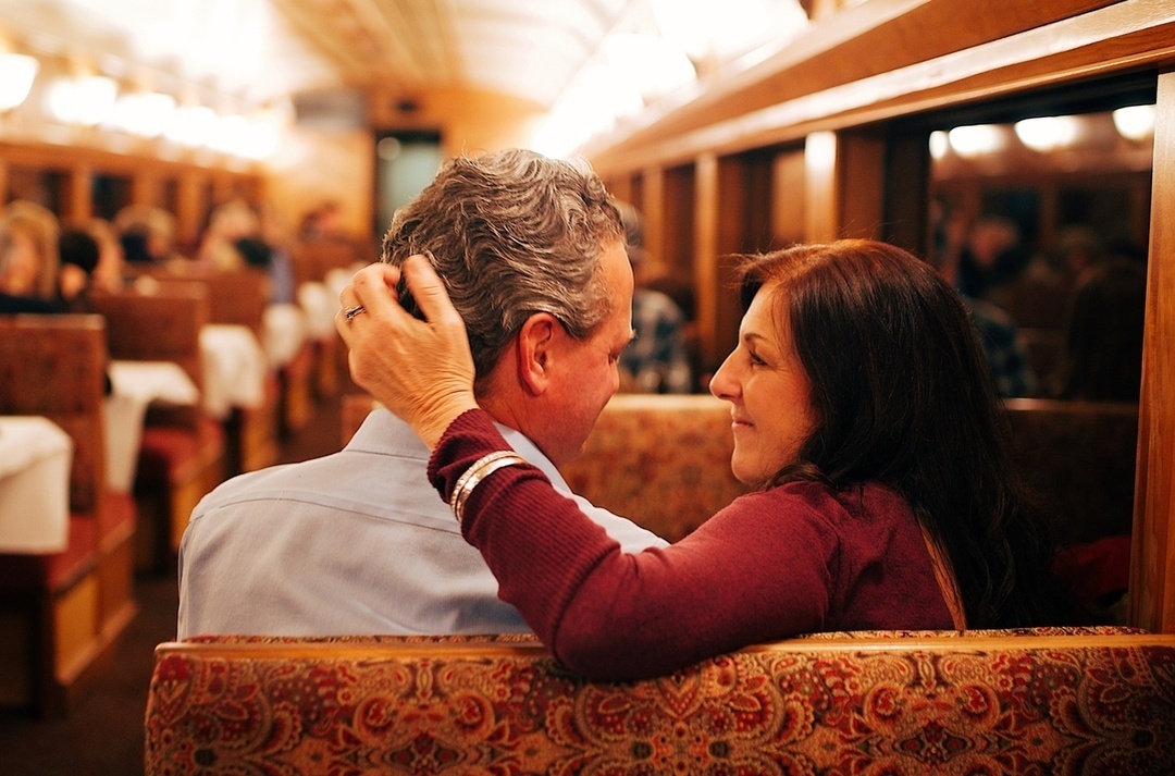 Couple sitting closely in a train, woman touching man's head affectionately.