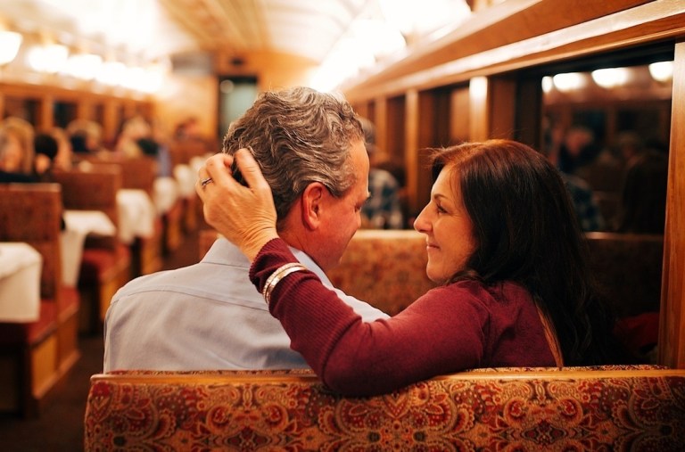 Couple sitting closely in a train, woman touching man's head affectionately.