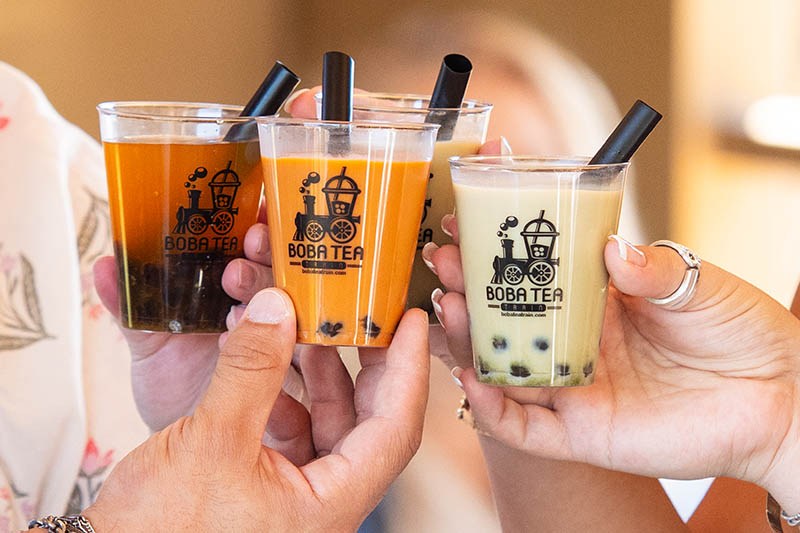 Hands holding three bubble tea cups with straws.