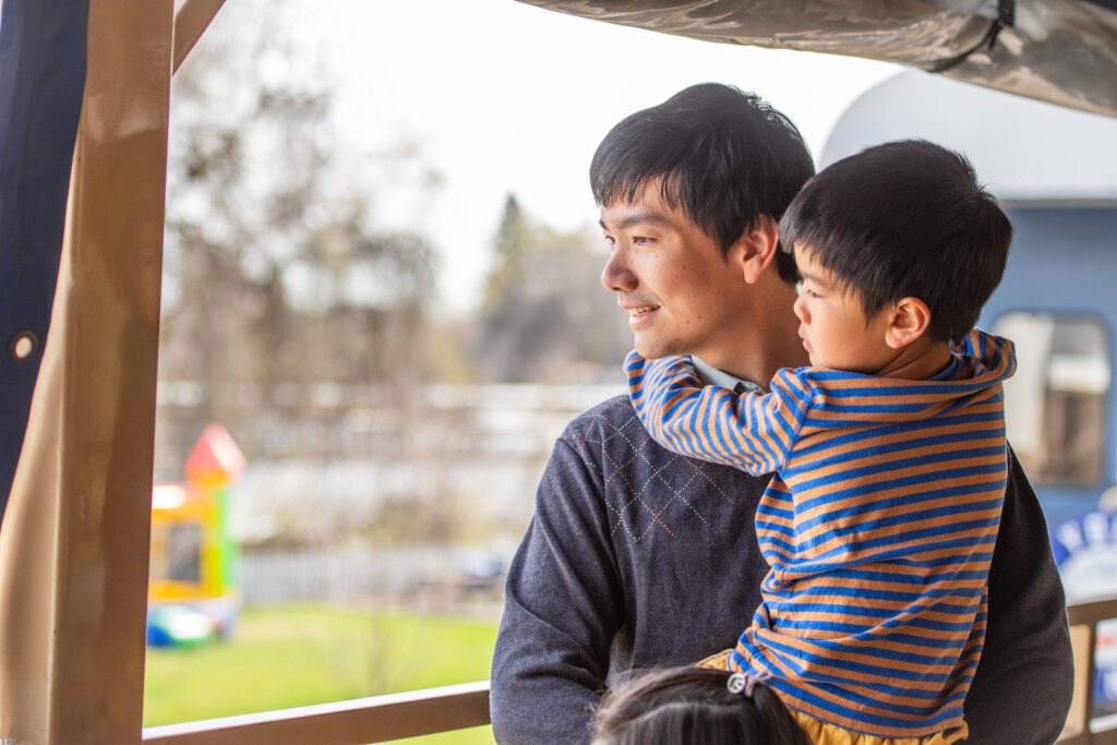 Man holding child on balcony, both looking outside.