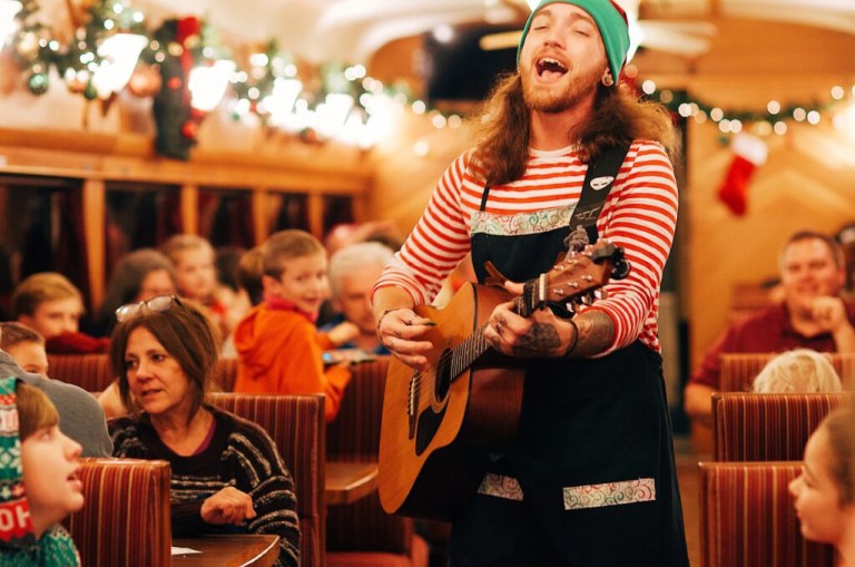 Person in festive attire singing and playing guitar in a decorated, crowded room.