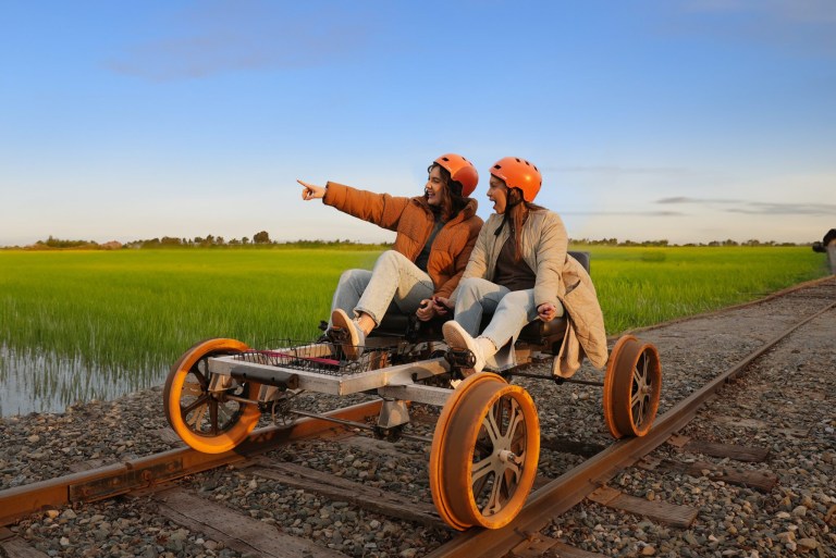 Two people on a rail bike pointing at green fields under a blue sky.