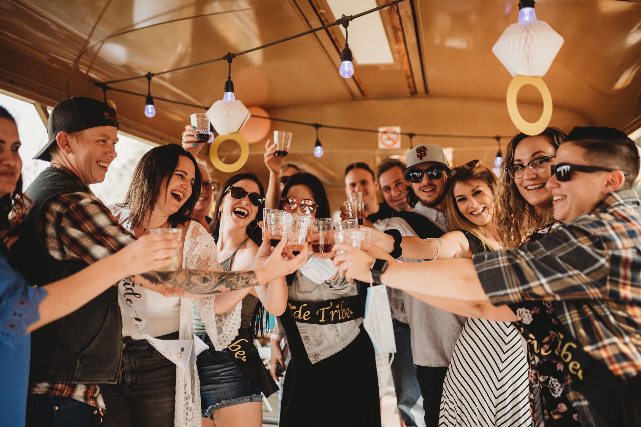 Group of people toasting drinks inside a decorated space with hanging lights.