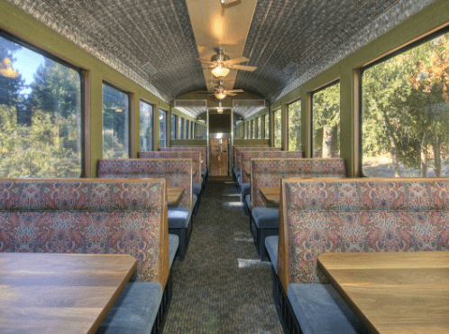 Interior of a vintage train dining car with wooden tables and patterned seats.