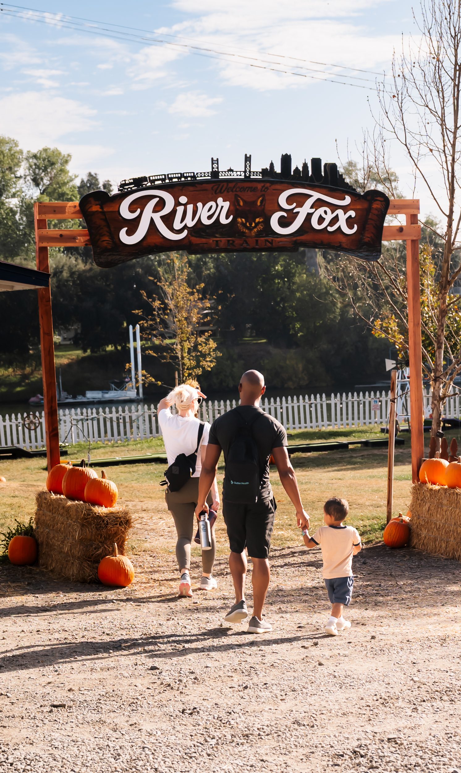 Family walking under a 'River Fox' sign with pumpkins around.