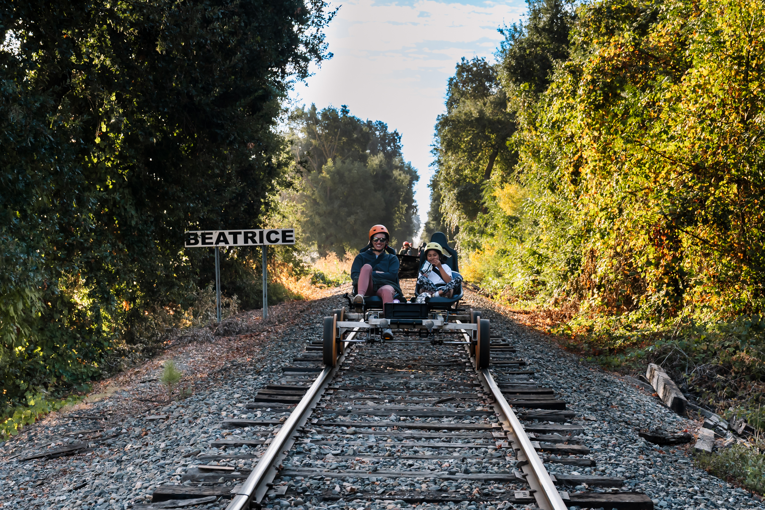 People riding a rail cart on train tracks beside trees.