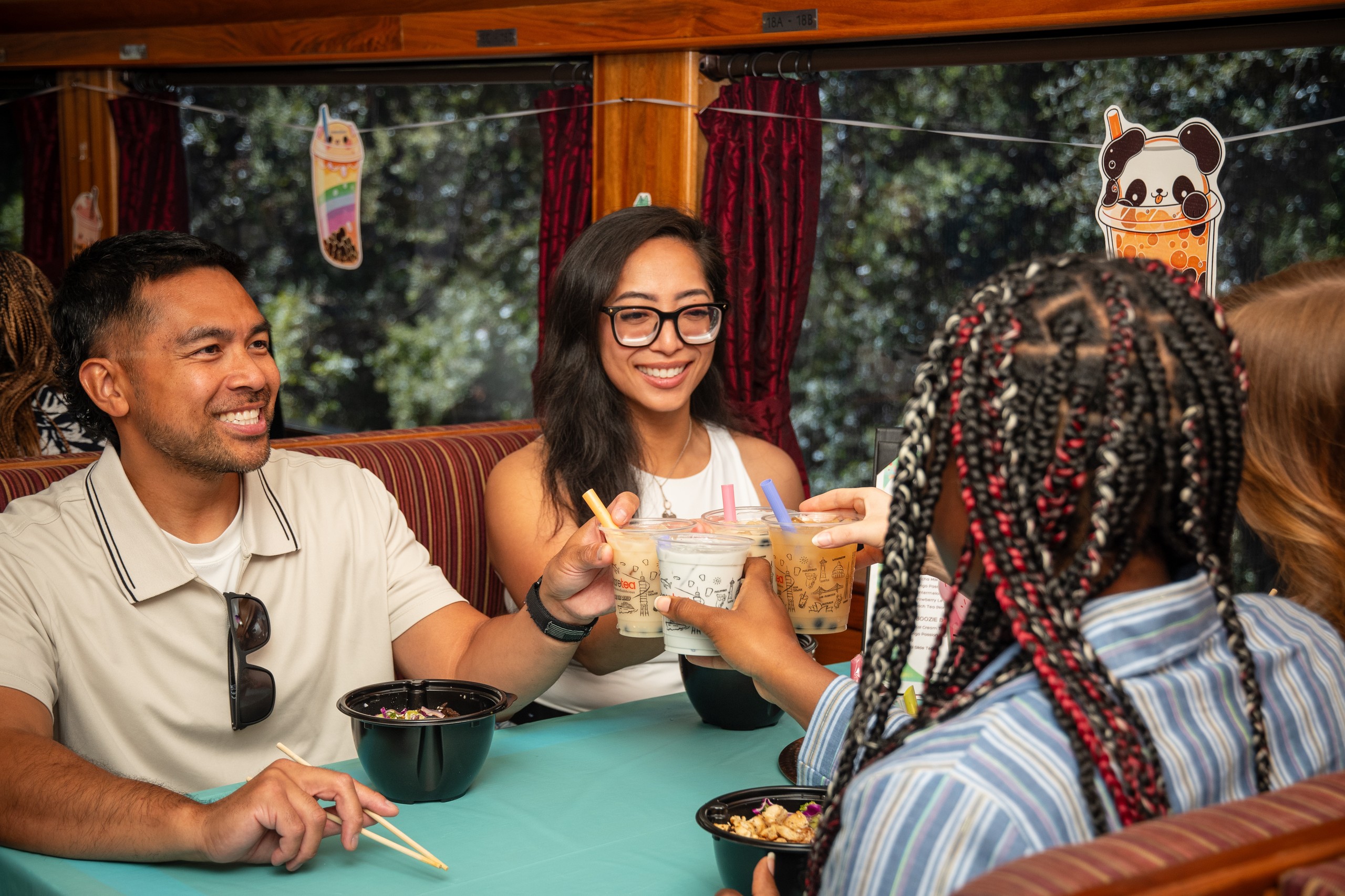 Group enjoying bubble tea and noodles on a train with panda decor.